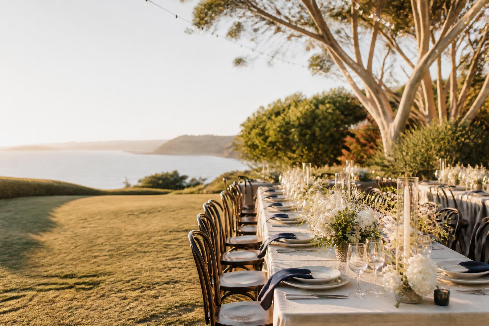 A coastal wedding reception set with long linen tables and white flowers